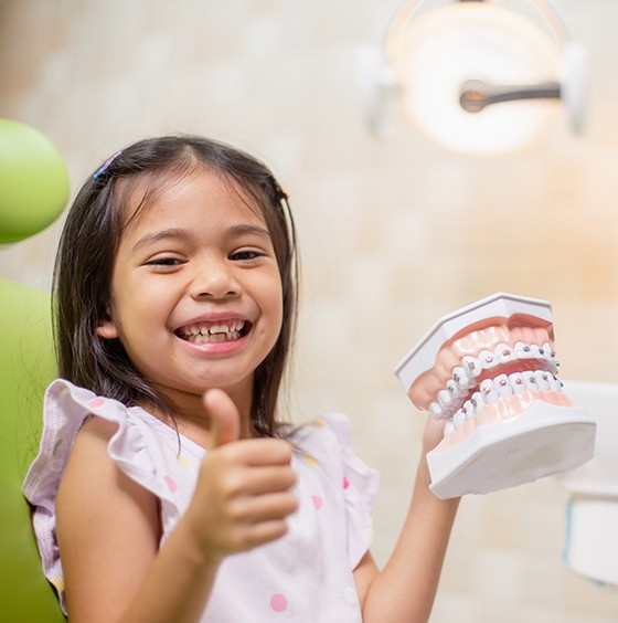 Smiling child holding a braces model during an orthodontic consultation